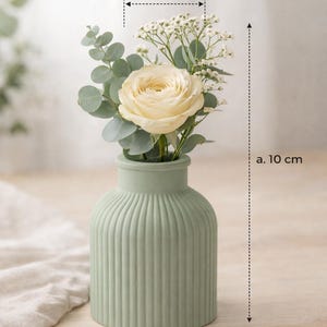 Könnte beinhalten: Ein Set aus drei Keramikbechern mit gesprenkelter, matter Oberfläche. Die Becher sind in Creme-, Hellgrau- und Dunkelgrautönen gehalten. Jeder Becher hat ein schlichtes, minimalistisches Design und einen abgerundeten Henkel.