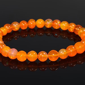May include: A vibrant orange beaded bracelet. The bracelet is composed of numerous round, polished beads. The beads have a translucent quality, with a warm, glowing appearance. The bracelet is displayed against a dark background, highlighting its color.