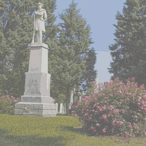 Könnte beinhalten: Ein steinernes Denkmal für den Bürgerkrieg mit einer Statue eines Soldaten, der ein Gewehr hält, vor dem Hintergrund von Bäumen und blauem Himmel. Das Denkmal ist mit Text beschriftet und von grünem Gras und rosa blühenden Büschen umgeben.