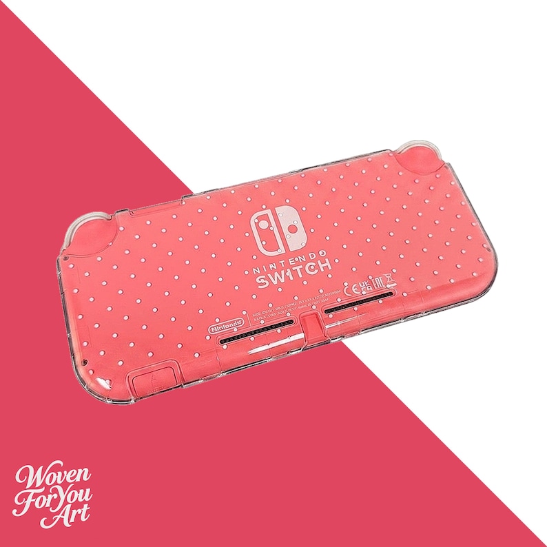 May include: A coral-colored Nintendo Switch Lite handheld gaming console case featuring a white polka dot pattern. The clear protective shell displays the Nintendo Switch logo and branding text on the back, along with visible ventilation slots.