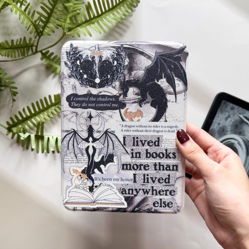 Pu&ograve; includere: Una custodia Kindle bianca e grigia con un'illustrazione di drago nero e il testo "I lived in books more than I lived anywhere else." La custodia presenta anche altre grafiche e citazioni a tema drago.
