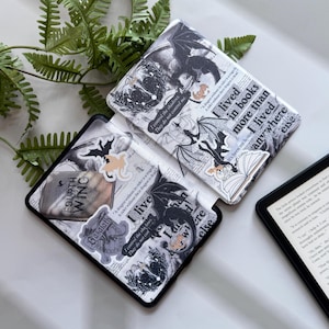 Pu&ograve; includere: Due custodie per e-reader in bianco e nero con disegni di draghi e testo. Una custodia &egrave; aperta, rivelando lo schermo dell'e-reader. Le custodie presentano illustrazioni di draghi, testo ed elementi decorativi. Il testo include frasi come "I lived in books" e "Fourth Wing."