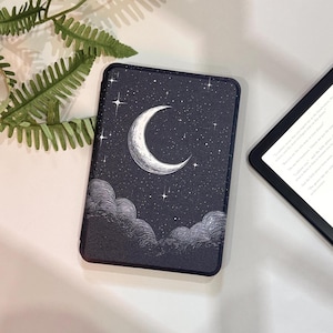 May include: A dark blue e-reader case featuring a crescent moon and stars design. The celestial illustration includes a white crescent moon, stars, and clouds. The case is rectangular and has a black border. A second e-reader is partially visible.