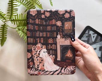 May include: A decorative Kindle case featuring a whimsical illustration of a ghost relaxing in a floral armchair in front of a fireplace and bookshelf. The case has a dark background with rose and floral accents.