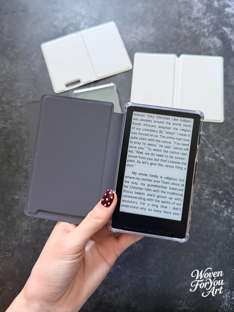 May include: An e-reader device with a clear protective case and a dark gray folding cover. The screen displays text about religious history and cultural beliefs. Two additional white folding covers are positioned in the background.