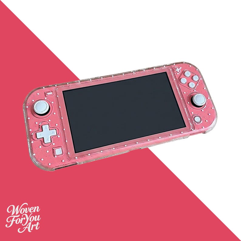 May include: A handheld gaming console featuring a pink shell with a white polka dot pattern and a clear protective case. The device includes a black screen, white control buttons, and two analog sticks. The text Woven For You Art is visible.