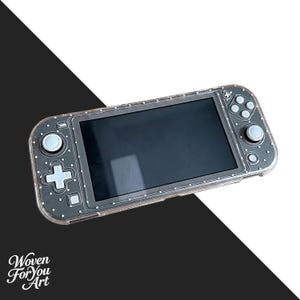 May include: A handheld gaming console encased in a clear, glittery protective shell featuring a pattern of small white dots. The device has a black screen, light gray buttons, and dual analog sticks. The text Woven For You Art appears in the corner.