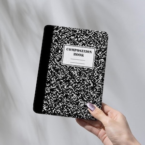 May include: A black and white composition book with the words "COMPOSITION BOOK" on the front. The cover has a speckled pattern. The book is held in front of a light gray background.