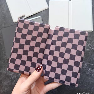 May include: A rectangular folding case featuring a dark brown and light mauve checkered pattern. The case is shown in an open position, revealing two symmetrical panels. In the background, two additional plain white rectangular cases are visible.