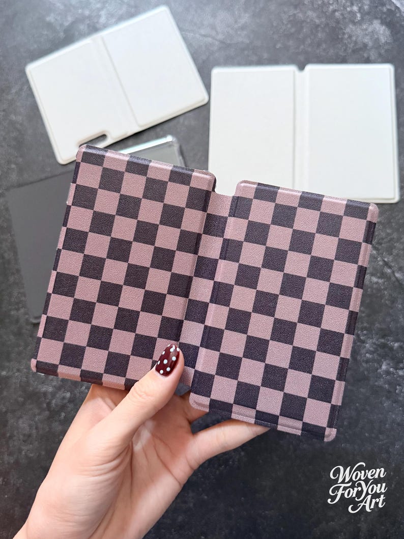 May include: A rectangular folding case featuring a dark brown and light mauve checkered pattern. The case is shown in an open position, revealing two symmetrical panels. In the background, two additional plain white rectangular cases are visible.