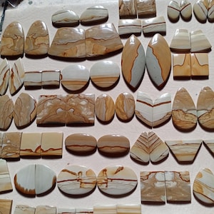 以下が含まれることがあります： 様々な形の磨かれた天然石カボションのコレクション。楕円形、涙型、長方形など。石はベージュ、茶色、クリーム色の暖色系の色合いで、独特の縞模様があります。いくつかの石は対になっており、対称的なデザインになっています。