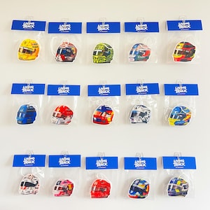 May include: Fifteen individual air fresheners shaped like racing helmets, each packaged in a clear plastic sleeve with a blue Living Track header card. The helmets feature various colorful designs, logos, and patterns representing different racing teams.
