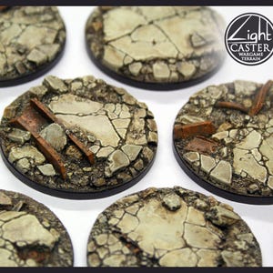 May include: A collection of circular wargame terrain bases, each with a detailed, cracked stone effect. The bases are predominantly grey, brown, and beige, with some featuring small debris. The Light Caster Wargame Terrain logo is displayed on the image.