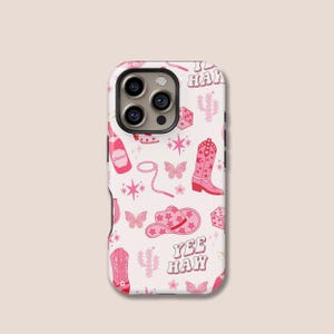 Puede incluir: Una funda de teléfono blanca con un diseño rosa con temática de vaquero. El diseño incluye botas de vaquero, sombreros, mariposas, cactus, dados y las palabras "Yee Haw". La funda tiene un recorte para la cámara de triple lente.