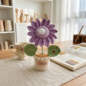 May include: A handmade crochet flower in a small pot. The flower has purple petals and a white center. Green leaves and a small ladybug accent the flower. The pot is beige with a "HANDMADE" tag.