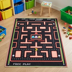 May include: A rectangular area rug featuring a black background with a classic arcade maze pattern in peach, including the text 1UP, HIGH SCORE 10000, 2UP, GAME OVER, and FREE PLAY. The design includes pixelated ghosts and a yellow character icon.