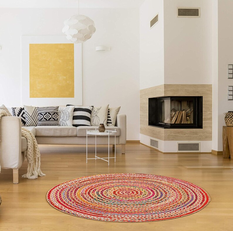 Puede incluir: Una alfombra redonda trenzada multicolor, con c&iacute;rculos conc&eacute;ntricos rojos, amarillos y azules. La alfombra est&aacute; colocada sobre un suelo de madera en un sal&oacute;n. El di&aacute;metro de la alfombra es de aproximadamente 152 cm.