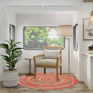 Puede incluir: Toma interior de una cocina y zona de estar blancas y luminosas. Una alfombra redonda multicolor se encuentra debajo de una silla de madera. Tambi&eacute;n se ven una l&aacute;mpara de pie alta y una planta en maceta. Una mesa peque&ntilde;a y una estampa bot&aacute;nica enmarcada completan la escena.