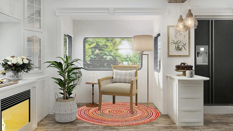 Puede incluir: Toma interior de una cocina y zona de estar blancas y luminosas. Una alfombra redonda multicolor se encuentra debajo de una silla de madera. Tambi&eacute;n se ven una l&aacute;mpara de pie alta y una planta en maceta. Una mesa peque&ntilde;a y una estampa bot&aacute;nica enmarcada completan la escena.