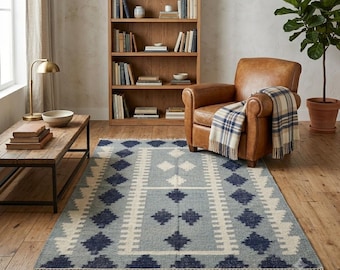 May include: A rectangular area rug featuring a light blue background with a repeating dark blue diamond pattern and white geometric borders. The rug has short fringe detailing along the short edges and is positioned on a wooden floor.