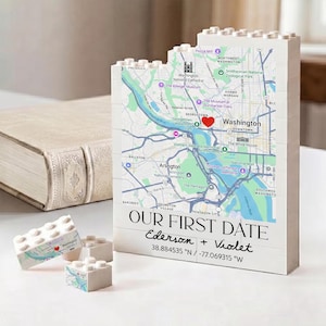 May include: A white building block display featuring a map of Washington D.C. with a red heart icon. The text reads OUR FIRST DATE, Ederson + Violet, and the coordinates 38.884535 N / -77.069315 W. Two smaller matching blocks are placed in front.