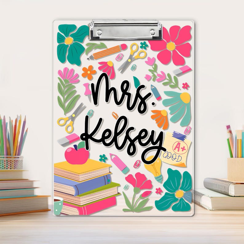 May include: A clear clipboard with a metal clip, decorated with colourful flowers, pencils, scissors, and books. The name "Mrs. Kelsey" is written in black script. A+ grade is shown on a yellow paper.