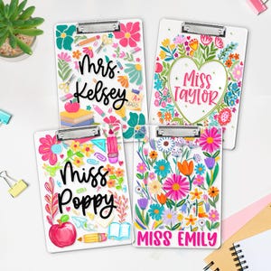 May include: Four white clipboards with floral designs and teacher names: Mrs. Kelsey, Miss Taylor, Miss Poppy, and Miss Emily. Each clipboard features colourful flowers, school supplies, and a silver clip.