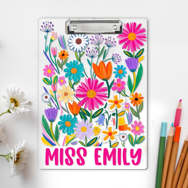 May include: A white clipboard adorned with a colourful floral pattern, including pink, orange, blue, and yellow flowers. The text "MISS EMILY" is in pink. A silver clip secures the paper. Pencils are in the background.