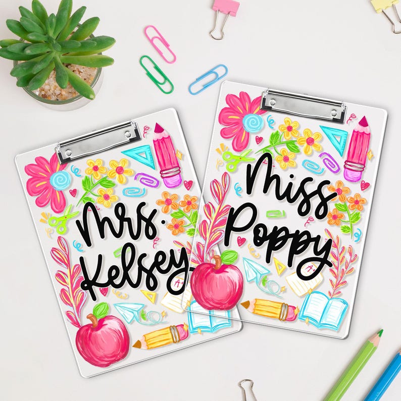 May include: Two white clipboards with colourful floral and school-themed designs. One clipboard says "Mrs. Kelsey" and the other says "Miss Poppy" in black script. The designs include pink flowers, pencils, and apples.