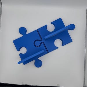May include: A blue puzzle piece shelf, composed of four interlocking pieces. The shelf is a vibrant blue color and features two horizontal supports for displaying items. The design is simple and modern, suitable for various decor styles.
