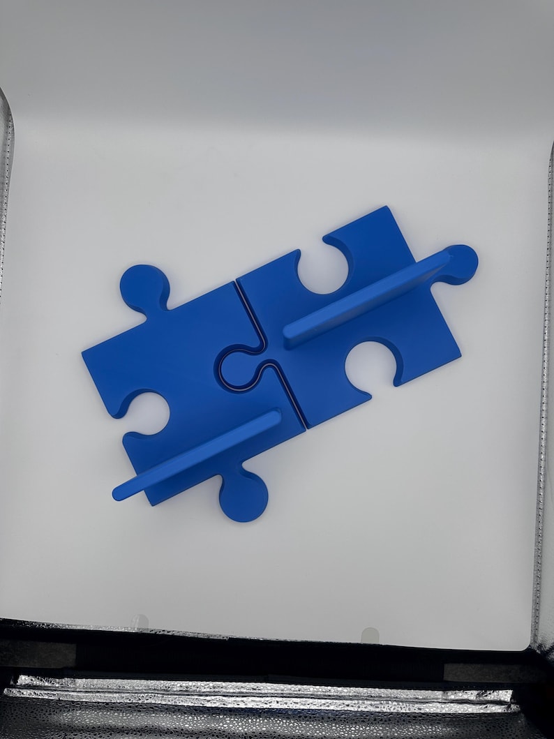 May include: A blue puzzle piece shelf, composed of four interlocking pieces. The shelf is a vibrant blue color and features two horizontal supports for displaying items. The design is simple and modern, suitable for various decor styles.