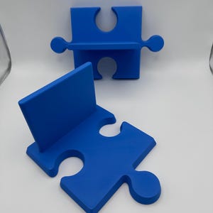 May include: Two blue puzzle piece-shaped shelves. One is upright, and the other is lying flat. The shelves are a solid, vibrant blue color and have a smooth, matte finish. The design is simple and modern, suitable for home decor.