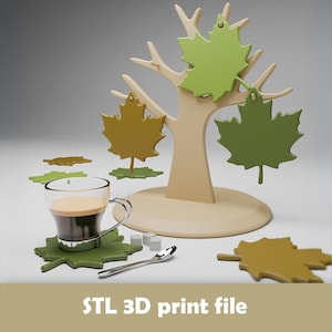 May include: A beige tree-shaped coffee cup holder with green and yellow maple leaf accents. A glass cup with coffee sits on a green leaf-shaped coaster. A small spoon and sugar cubes are also present. The text "STL 3D print file" is at the bottom.