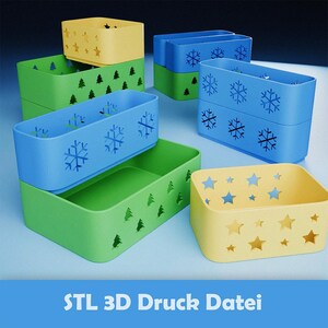 Op de afbeelding: Een verzameling kleurrijke, stapelbare opbergbakken in geel, groen en blauw. De bakken hebben uitgesneden ontwerpen van sterren, sneeuwvlokken en bomen. De tekst "STL 3D Druck Datei" staat onderaan.