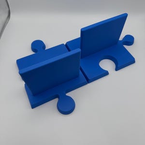 May include: A blue puzzle piece-shaped desk organizer. The organizer is made of four interlocking pieces, with two vertical dividers. The design is a vibrant blue color, and the pieces fit together to form a functional desk accessory.