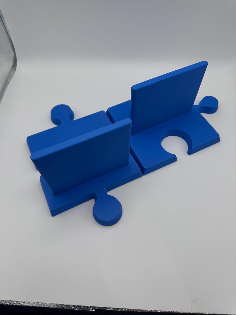 May include: A blue puzzle piece-shaped desk organizer. The organizer is made of four interlocking pieces, with two vertical dividers. The design is a vibrant blue color, and the pieces fit together to form a functional desk accessory.