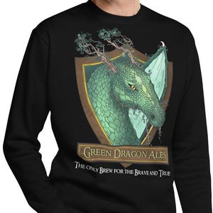 May include: Black sweatshirt with a green dragon illustration on the front. The dragon is set within a shield shape, with the words "Green Dragon Ales" and "The Only Brew for the Brave and True" below. The dragon has a textured, scaled appearance.