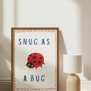 Peut inclure: Une affiche encadrée avec une coccinelle rouge à pois noirs et l'inscription "SNUG AS A BUG" en bleu. L'affiche a un fond blanc et un cadre marron avec une bordure pointillée. Décoration murale.