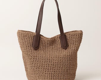 May include: A woven tote bag in a light brown color. The bag has two dark brown leather handles and matching leather accents at the top. The bag is made of a textured, woven material.