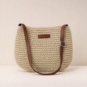 Pu&ograve; includere: Borsa a tracolla beige intrecciata con cinturini in similpelle marrone e una piccola toppa rettangolare. La borsa ha una forma arrotondata e una fibbia sul cinturino per la regolazione. La borsa &egrave; realizzata in materiale intrecciato.