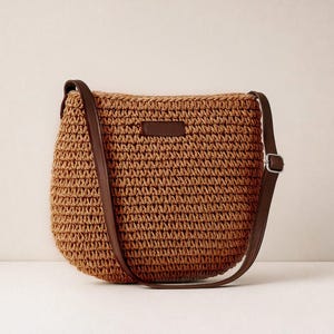 Pu&ograve; includere: Una borsa a tracolla marrone intrecciata con un cinturino in pelle marrone e una piccola toppa rettangolare in pelle. La borsa ha una forma arrotondata e una fibbia argentata sul cinturino. La borsa &egrave; realizzata in materiale intrecciato.