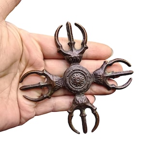 Peut inclure: Un objet rituel vajra en métal de couleur bronze en forme de croix, doté de quatre branches symétriques s'étendant à partir d'un moyeu central circulaire orné d'un motif de pétales de lotus et d'une série de petits points en relief.