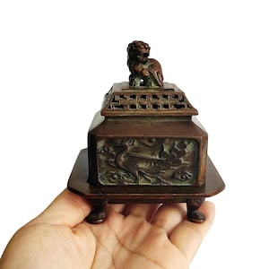 May include: A bronze incense burner with a lion figure on the lid. The rectangular body is adorned with carved bird and floral patterns. It rests on a small, square base with short legs, displaying an antique style.
