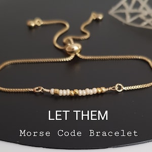 May include: Gold-toned Morse code bracelet with a sliding clasp. The bracelet features a series of small white and gold beads. The text "LET THEM Morse Code Bracelet" is displayed below the bracelet.