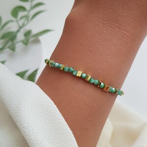 Puede incluir: Una delicada pulsera con peque&ntilde;as cuentas verdes redondas intercaladas con detalles rectangulares y en forma de flecha dorados. La pulsera se lleva en la mu&ntilde;eca, mostrando su dise&ntilde;o y contraste de color. La joya se presenta sobre un fondo neutro.