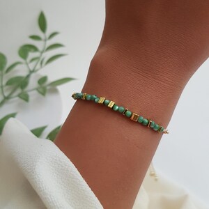 Puede incluir: Una delicada pulsera con peque&ntilde;as cuentas verdes redondas intercaladas con detalles rectangulares dorados. La pulsera est&aacute; ensartada en una fina cadena dorada y se muestra en una mu&ntilde;eca sobre un fondo neutro.