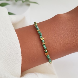Puede incluir: Una delicada pulsera con peque&ntilde;as cuentas redondas de color verde claro intercaladas con detalles rectangulares y en forma de flecha dorados. La pulsera se muestra en una mu&ntilde;eca, mostrando su dise&ntilde;o y color.