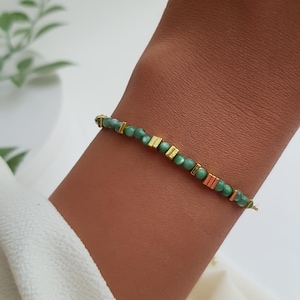 Puede incluir: Una delicada pulsera con peque&ntilde;as cuentas redondas verdes intercaladas con detalles rectangulares dorados. La pulsera est&aacute; ensartada en un fino alambre dorado. La joya se muestra en un brazo.