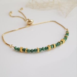 Puede incluir: Pulsera ajustable dorada con una delicada cadena. Cuenta con peque&ntilde;as cuentas verdes redondas y cuentas cuadradas doradas. Tiene un deslizador en forma de coraz&oacute;n para ajustar. Un accesorio elegante.