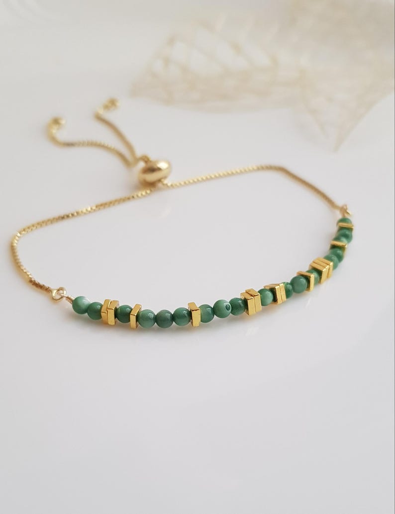 Puede incluir: Pulsera ajustable dorada con una delicada cadena. Cuenta con peque&ntilde;as cuentas verdes redondas y cuentas cuadradas doradas. Tiene un deslizador en forma de coraz&oacute;n para ajustar. Un accesorio elegante.